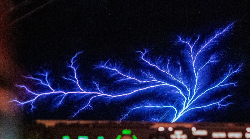 Electric blue branching lightning bolt against dark sky with warm city lights below