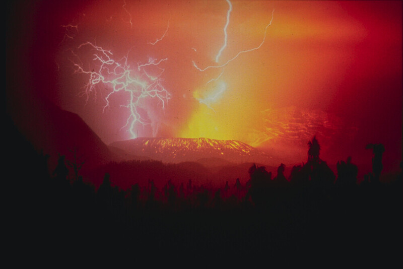 Dramatic storm scene with lightning bolts striking above a snow-capped volcanic mountain silhouetted against an intense orange and red sky
