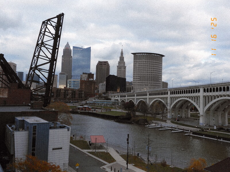 Cleveland skyline across the Cuyahoga River with a historic lift bridge and arched stone bridge