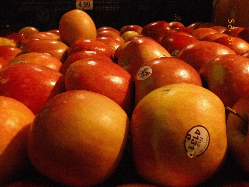 Pile of reddish-orange apples with produce stickers and price sign at farmer's market or grocery store