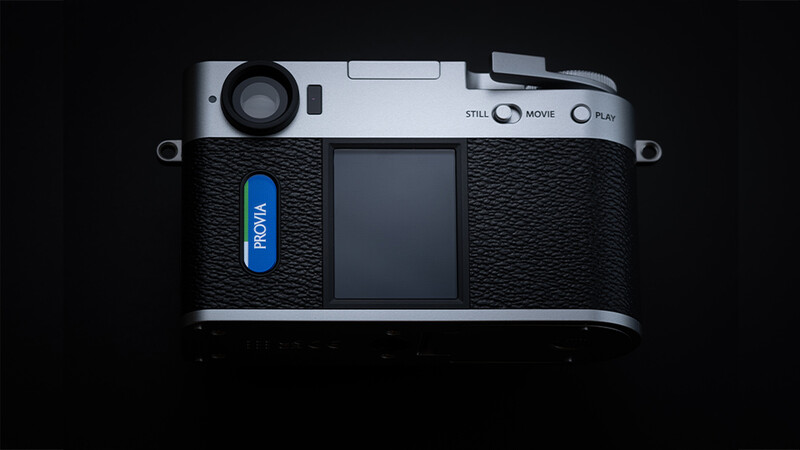 Top-down view of a silver and black rangefinder camera with blue grip and LCD screen