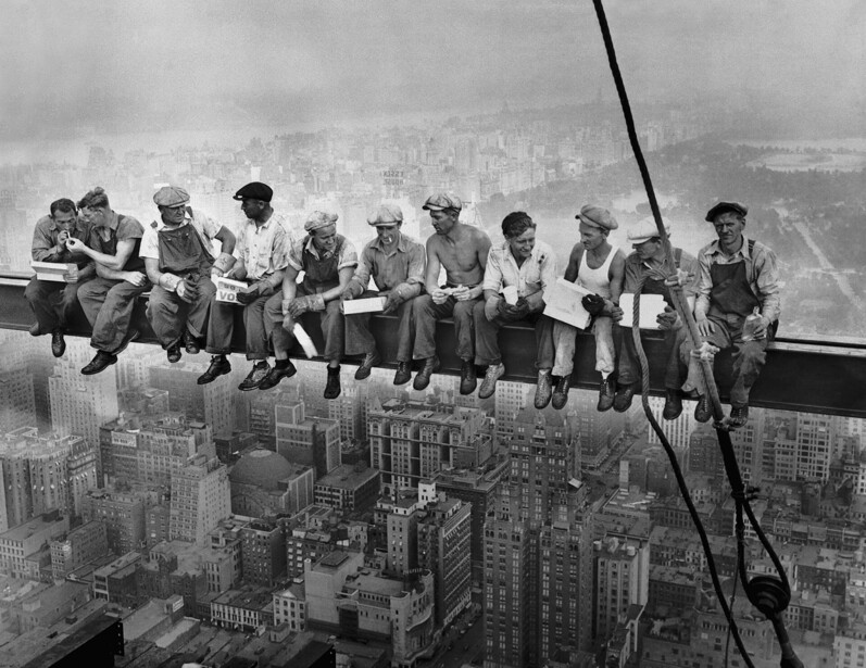 Workers sitting on steel beam high above Manhattan skyline during skyscraper construction