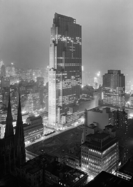 Nighttime cityscape with illuminated skyscraper towering above surrounding buildings in fog