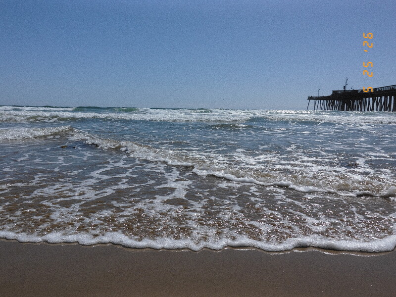 Ocean waves breaking on sandy beach with pier extending into the water under clear blue sky