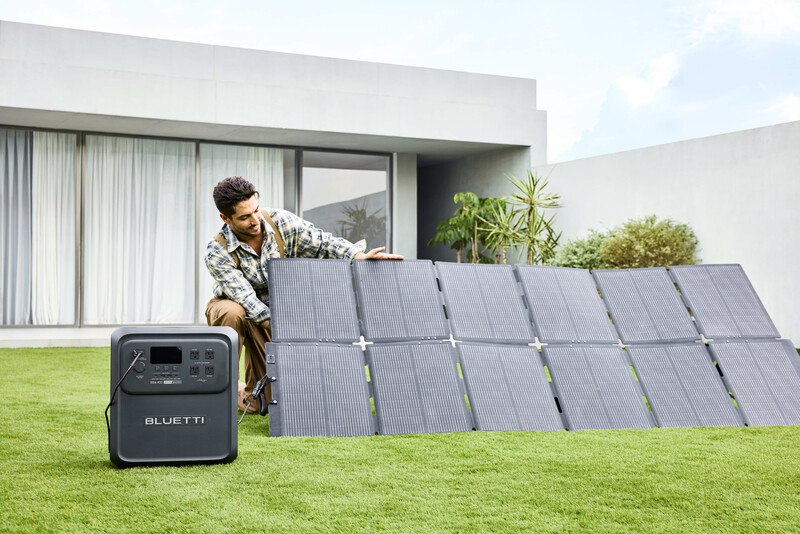 Man adjusting a portable solar panel array connected to a Bluetti power station on a residential lawn