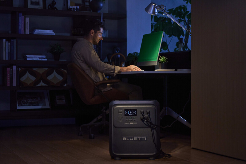 Photographer working at desk with portable power station and laptop in dimly lit home office