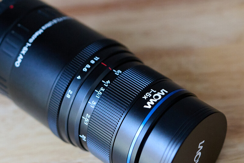 Close-up of a Laowa zoom lens showing focal length markings and focus ring on wooden surface