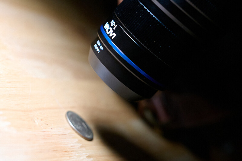 Camera lens with blue accent ring resting on wooden surface in soft natural light