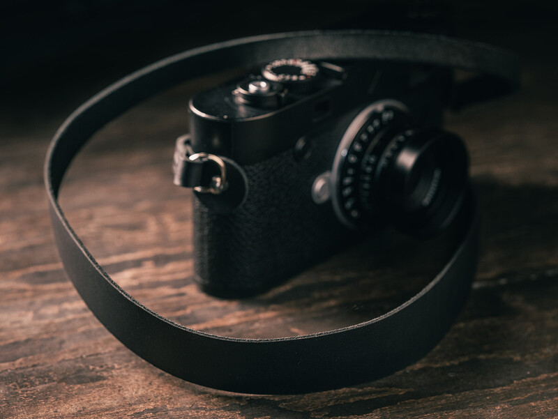 Black rangefinder camera with leather strap on wooden surface