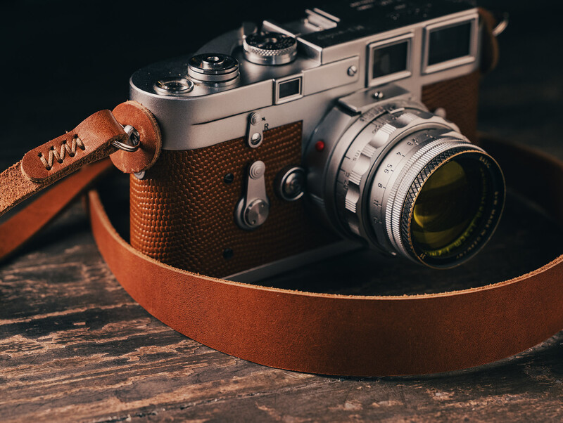 Vintage rangefinder camera with leather strap on wooden surface
