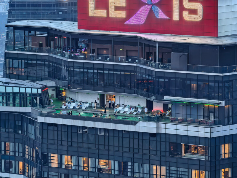 Multi-story modern building facade with illuminated windows and rooftop terrace activity