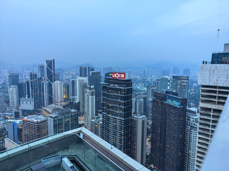 Urban cityscape at dusk with illuminated skyscrapers and distant mountains under blue twilight sky