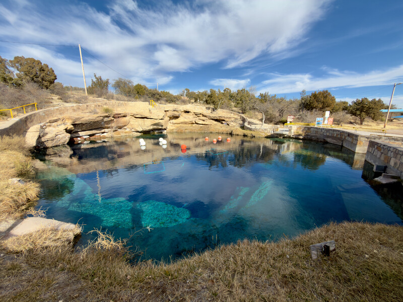 Crystal-clear turquoise pool reflecting blue sky with rocky shoreline and desert landscape