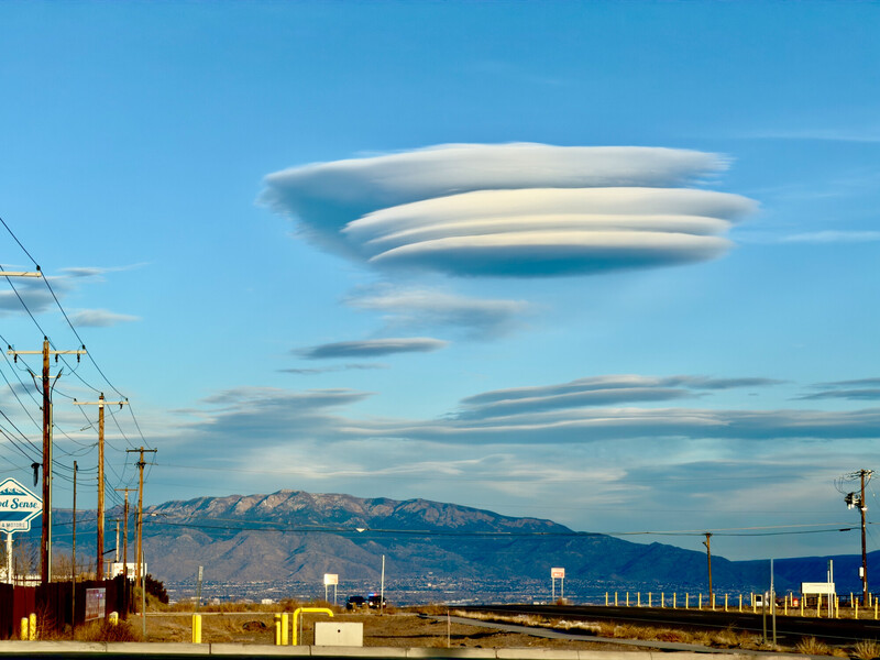 Lenticular clouds stacked in horizontal bands above an industrial landscape with mountains