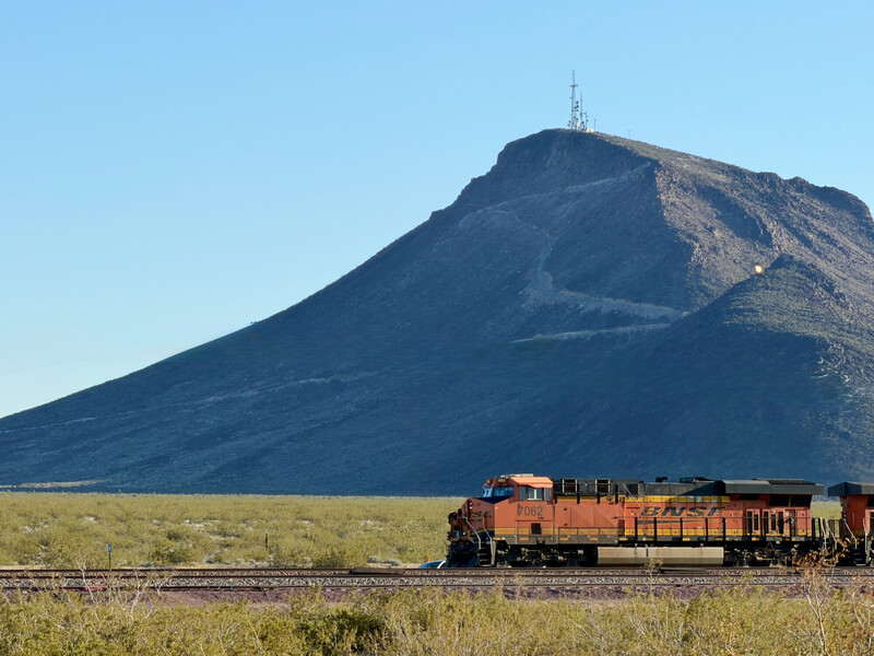 Union Pacific freight train passing through desert grassland with distinctive volcanic mountain peak in background