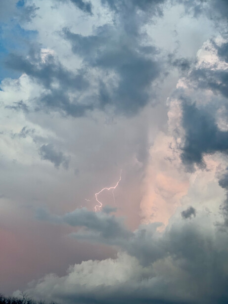 Towering cumulonimbus cloud with lightning bolt illuminating its interior structure against blue sky