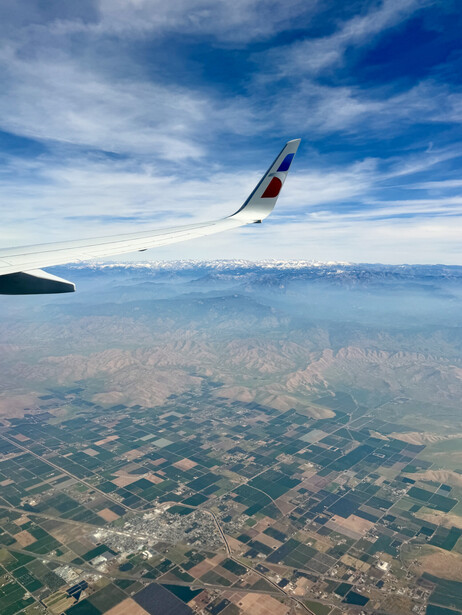 Airplane wing in flight above patchwork farmland and hazy valley landscape