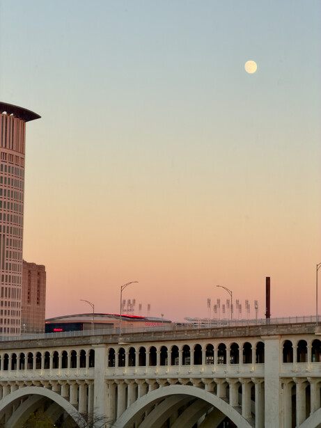 Full moon rising over an arched bridge at twilight with city buildings silhouetted against a pink-purple sky
