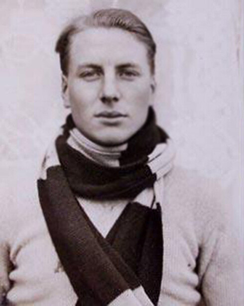Black and white portrait photograph of a young man with styled light hair wearing a dark sweater and scarf
