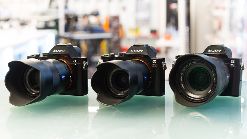Three Sony Alpha mirrorless cameras with different lenses displayed on a green surface