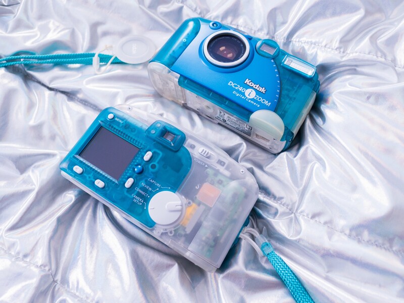 Two blue waterproof digital cameras displayed on white plastic material with blue lanyards attached