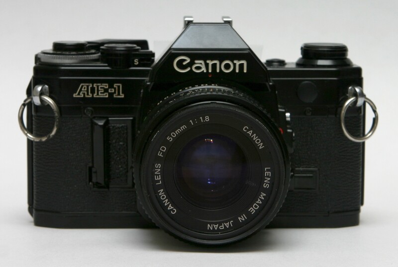 Canon AE-1 35mm SLR camera with 50mm f/1.8 lens, black body on white background