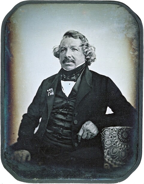 Hand-colored daguerreotype portrait of a middle-aged man with curled hair and mustache wearing formal black attire