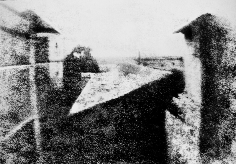 Grainy black and white photograph showing two figures observing a landscape from an elevated vantage point
