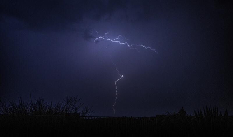 Lightning bolt illuminating dark storm clouds above a silhouetted landscape at night
