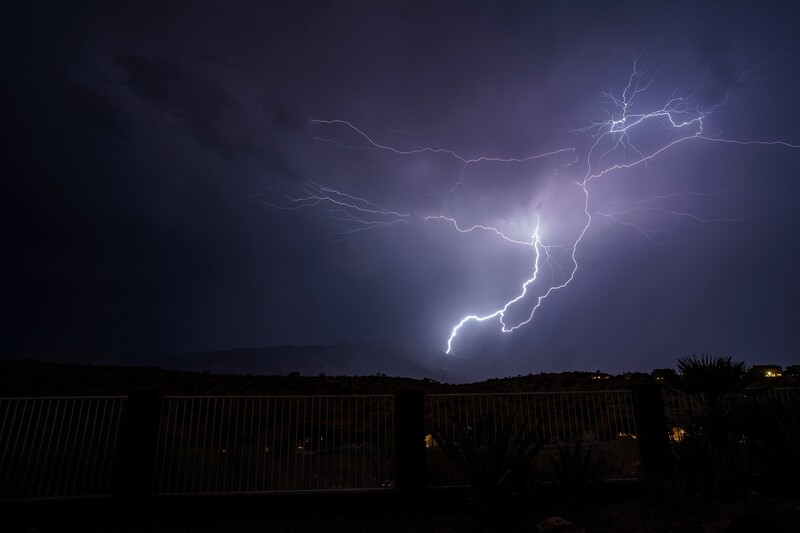 Lightning bolt striking across a dark night sky above silhouetted structures