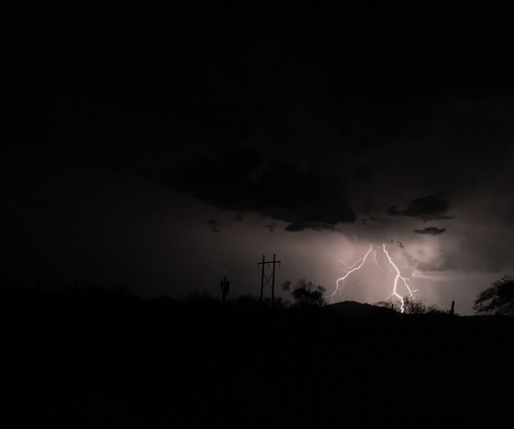 Lightning bolt illuminates dark storm clouds above silhouetted landscape with utility poles