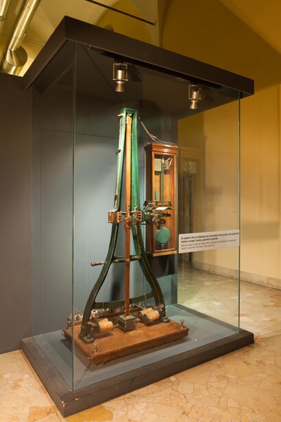 Antique mechanical device displayed in museum case with glass panels and overhead lighting