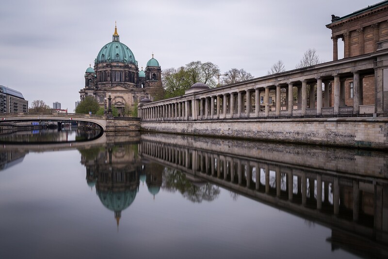 Berlin Cathedral's copper dome reflected in still river water with classical colonnade in foreground