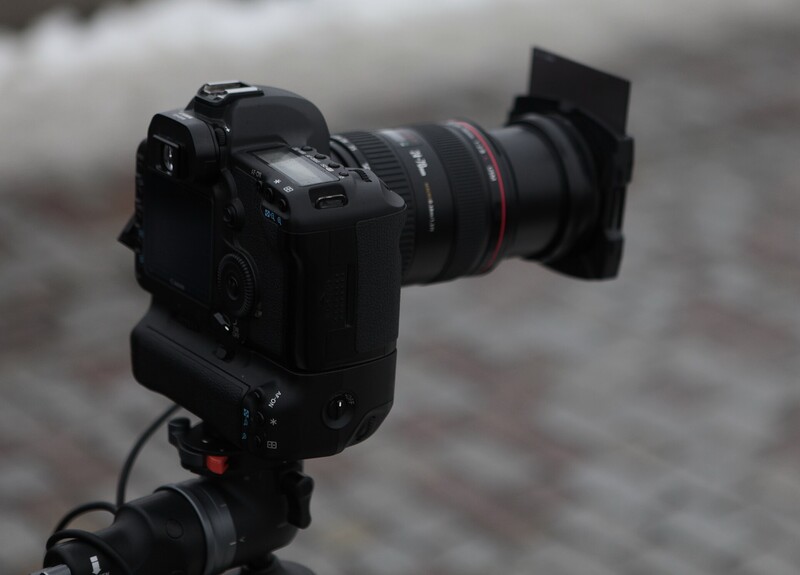 Professional DSLR camera with battery grip mounted on tripod, equipped with telephoto lens and LCD monitor