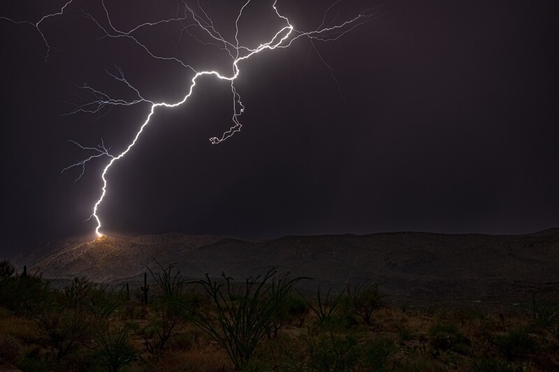 Lightning bolt striking desert landscape during nighttime thunderstorm