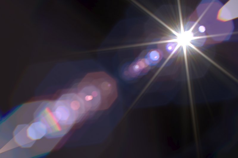 Bright light source creating lens flare with colorful bokeh circles on dark background