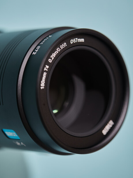 Macro view of a telephoto lens with blue accents and depth of field markings against light blue background