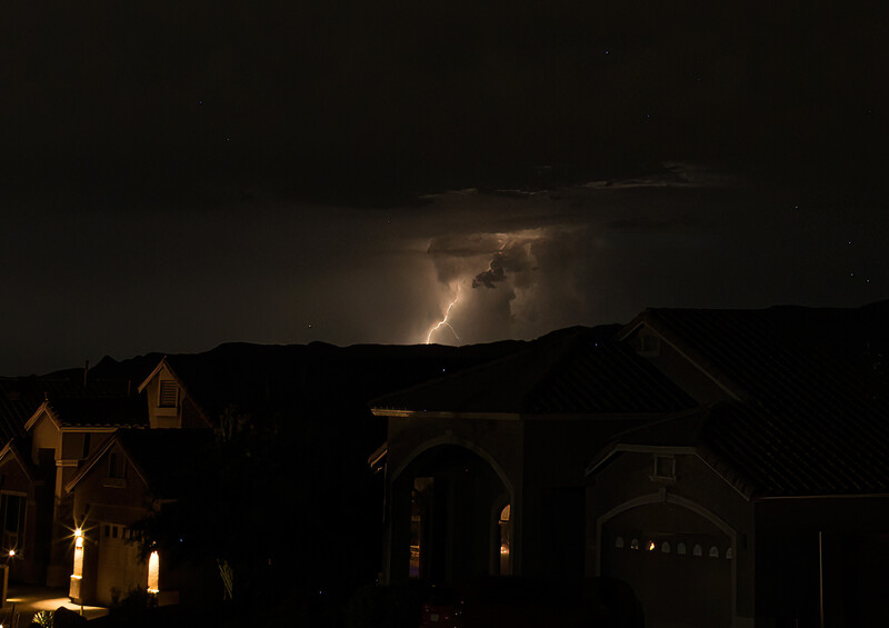 Lightning strike illuminating storm clouds above silhouetted residential houses at night