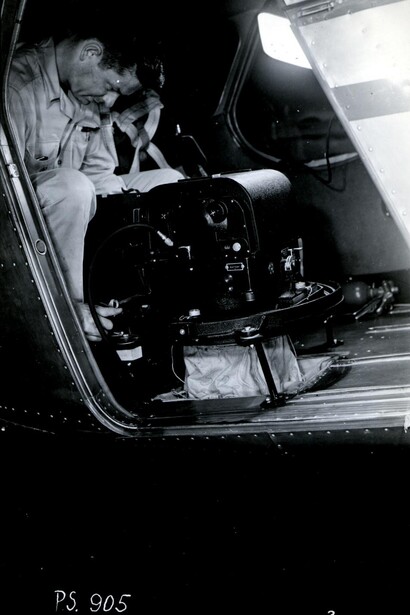 Black and white photograph of photographer inside vehicle cockpit with camera equipment