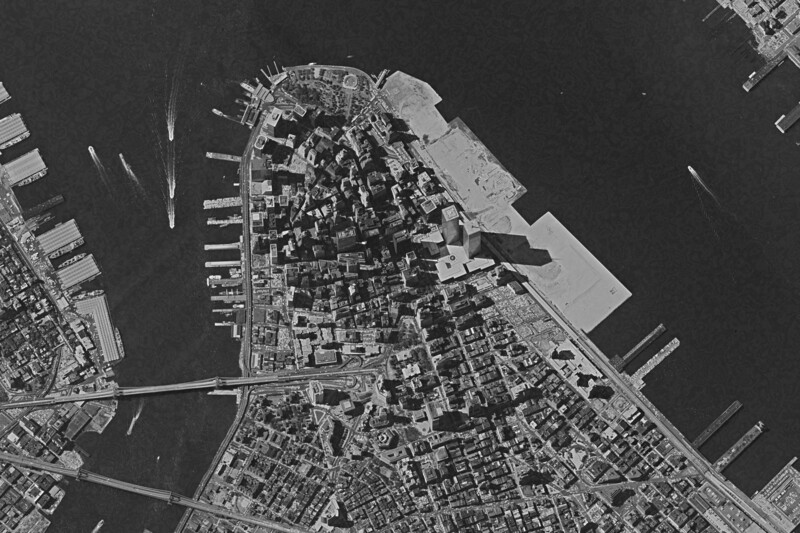 Aerial black and white photograph of a densely developed peninsula surrounded by water and docks