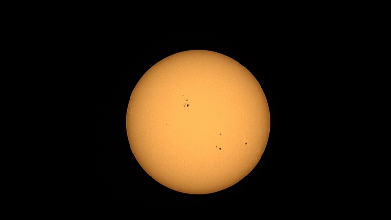 The Sun photographed against a black background, showing several dark sunspots across its orange-yellow surface