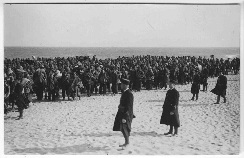 Large crowd gathered on a beach in formal dark clothing, photographed in black and white