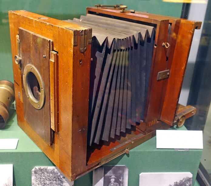 Vintage wooden field camera with bellows and brass fittings displayed in museum setting