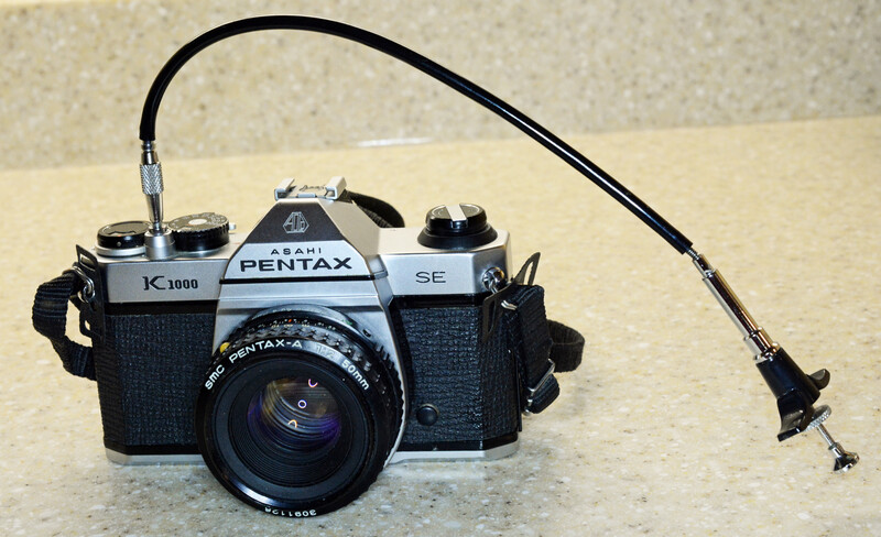 A mechanical cable release threaded into the shutter button of a Pentax K1000 SE
