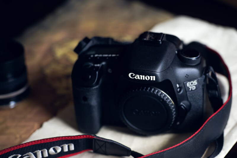 Canon EOS 7D camera body with red Canon neck strap on wooden surface