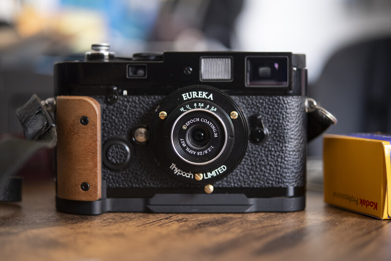 Eureka rangefinder camera with wooden grip and leather strap on wooden surface