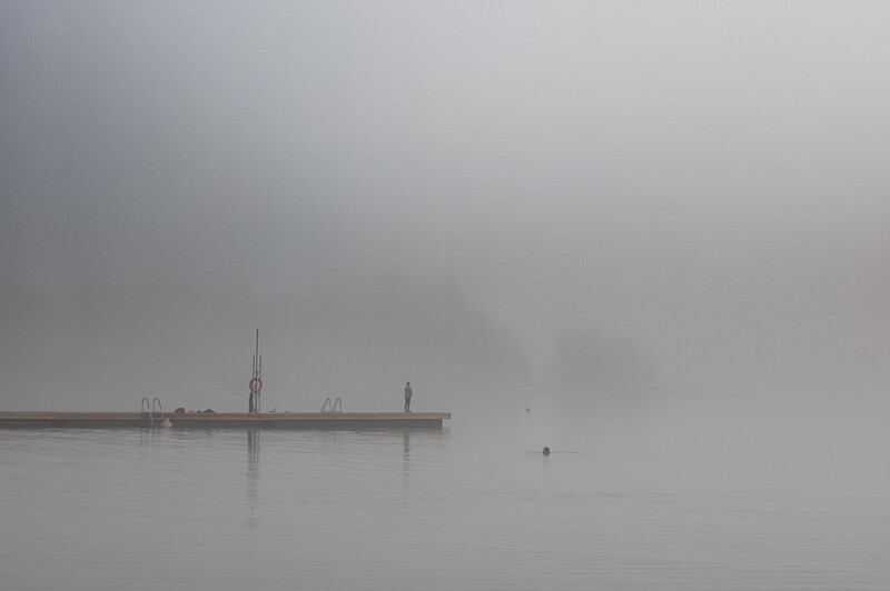 Minimalist foggy harbor scene with pier and solitary figure in dense mist