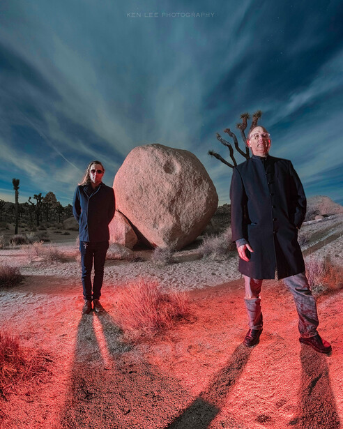 Two figures standing in infrared landscape with large boulder and dramatic sky