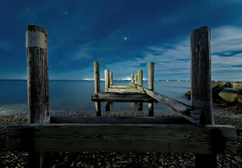 Weathered wooden pier pilings frame calm blue ocean waters under clear sky