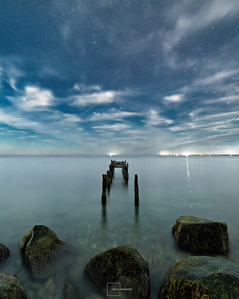 Abandoned wooden pier pilings in calm water under dramatic cloudy sky